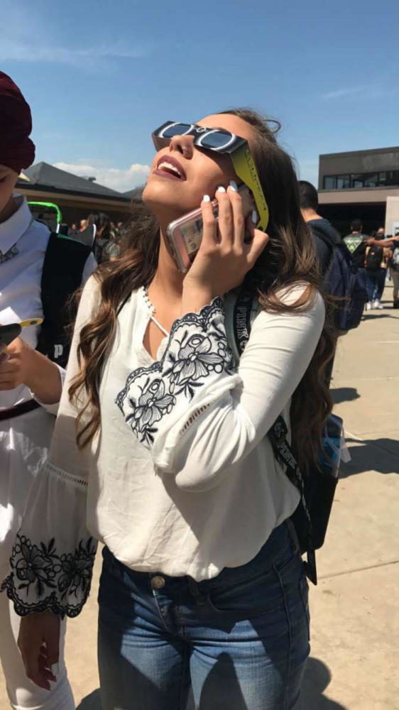 Junior Haylie Juhl shares the eclipse experience with a friend via her cell phone on Monday afternoon outside of Greeley West High School.