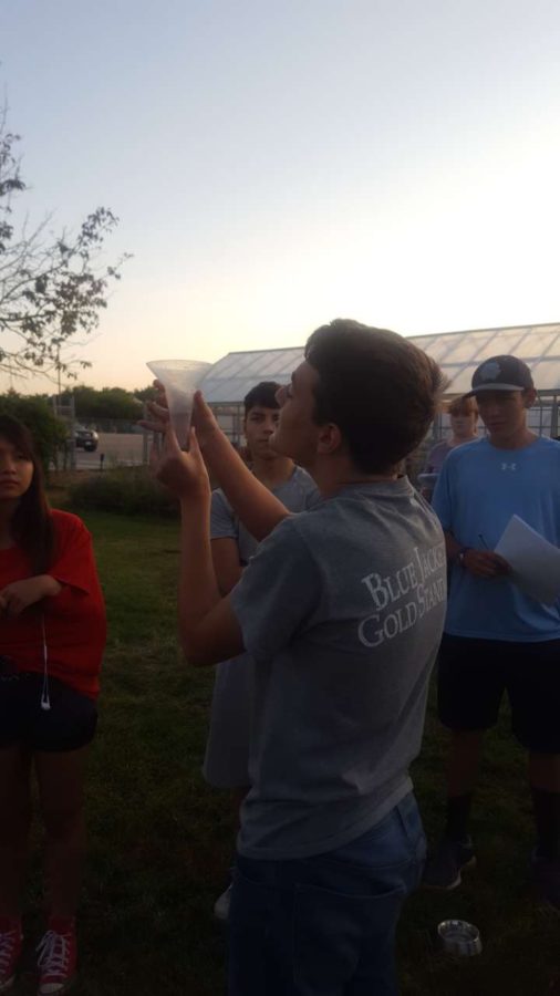 Noah Gentzler Mcpherson holds up a water sample toward the setting sun to determine how much water each area of a yard was getting from a sprinkler system.