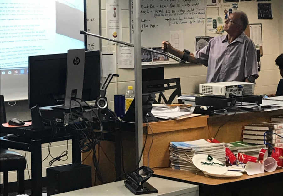 Mr. Richard Dufault points to the screen using his crutch during class on Monday.  Dufault returned to work last week after suffering a broken leg during a biking accident.  